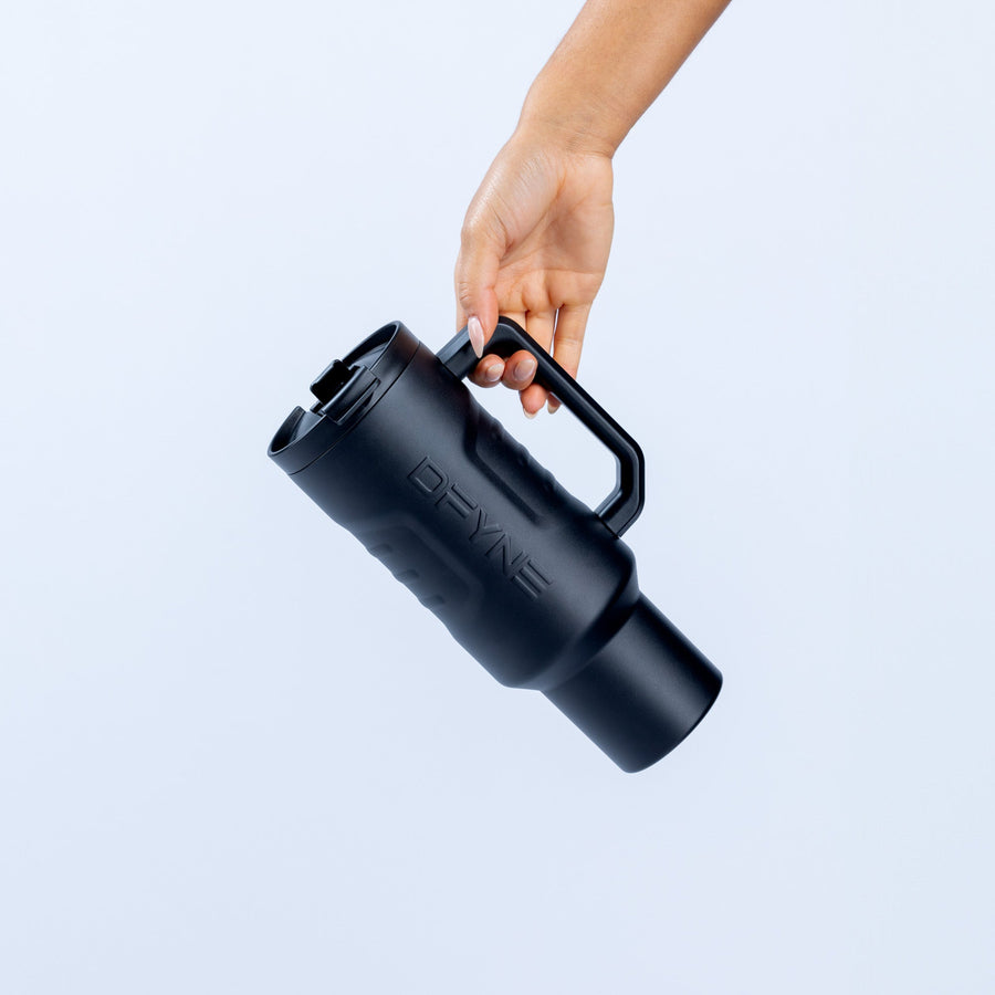 Insulated black drink tumbler held in hand, straw and lid visible
